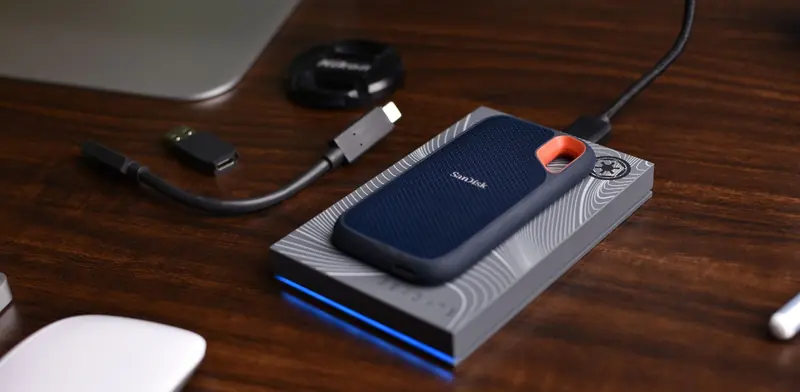 Portable external backup drive connected by cable on a wooden desk beside a computer