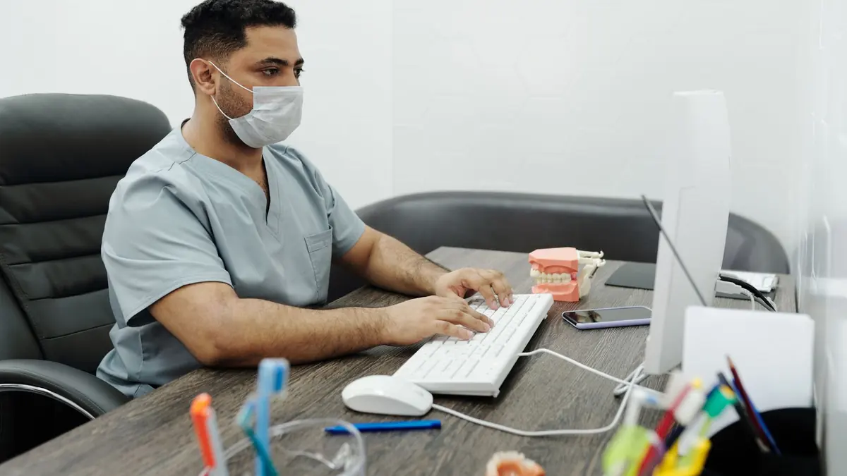 Dental clinic staff member in scrubs typing at a desktop computer in the clinic