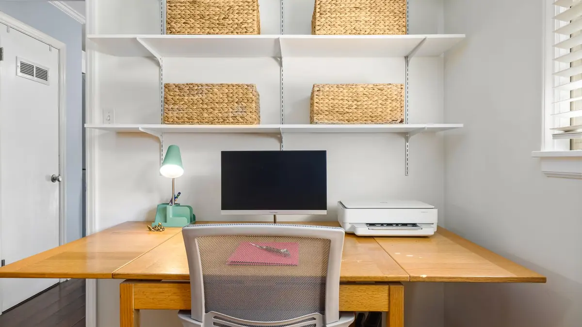 Home office desk with a desktop computer, printer and shelving in a bright room