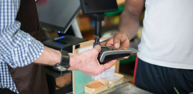 Customer paying by card on a terminal at a shop counter beside the till screen