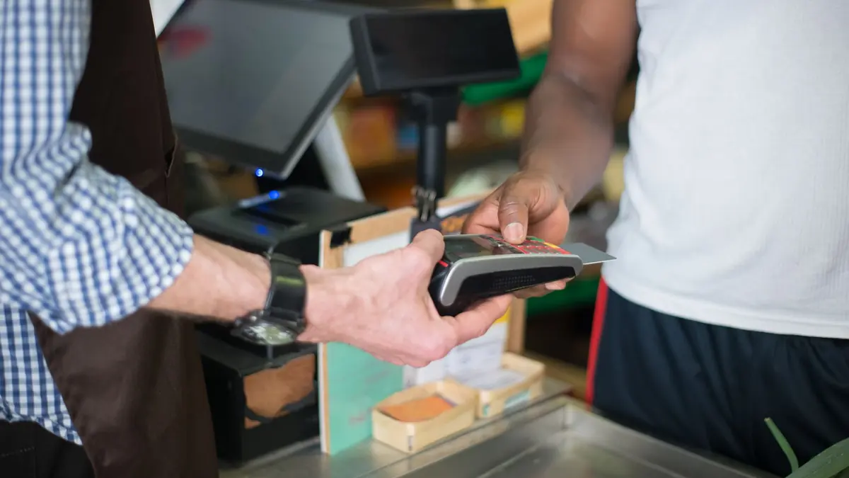 Customer paying by card on a terminal at a shop counter beside the till screen