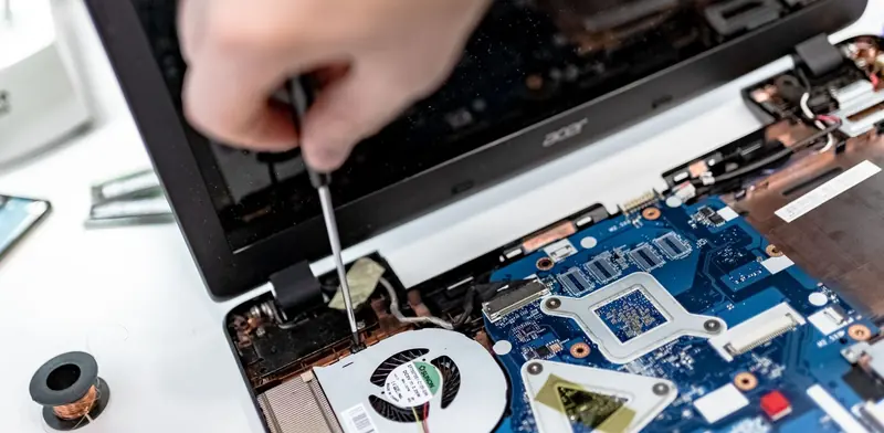 Technician using a small screwdriver on an opened laptop motherboard during repair