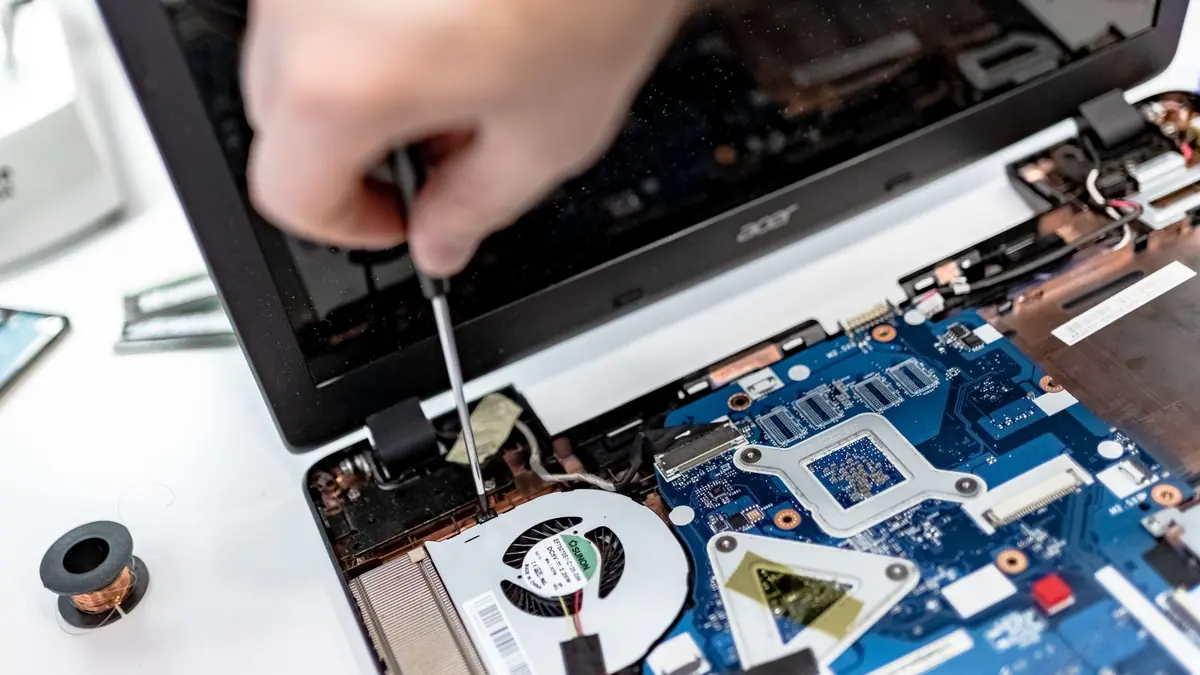 Technician using a small screwdriver on an opened laptop motherboard during repair