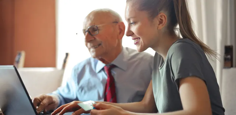 Young woman helping an older man use a laptop at home