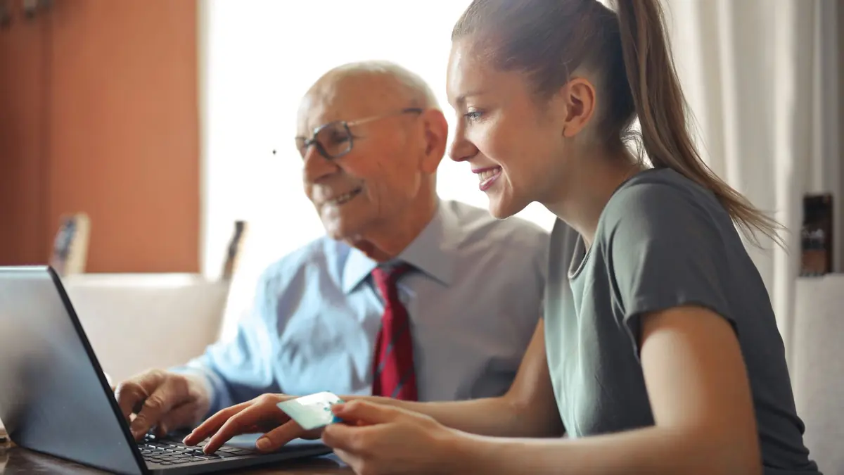 Young woman helping an older man use a laptop at home