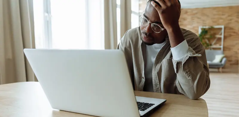Worried man holding his head while looking at a problem on his laptop